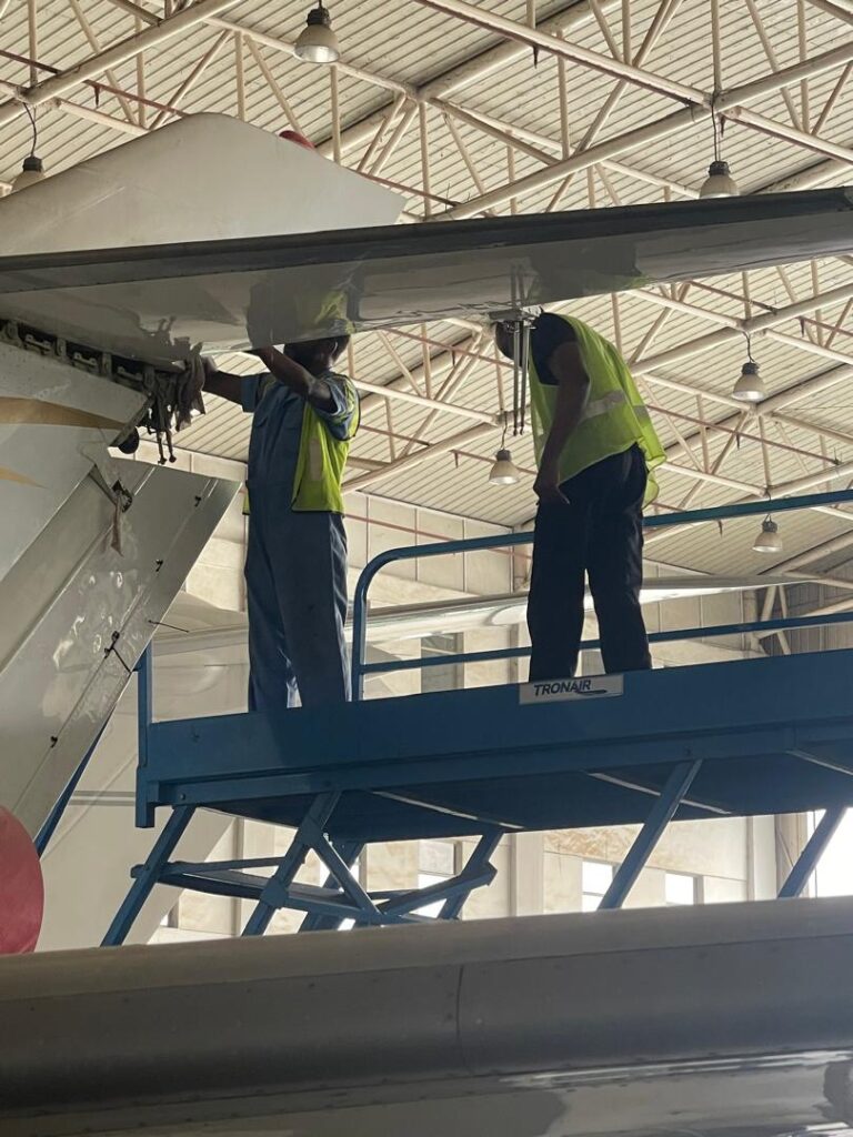 Two DJSD technicians working from an elevated platform beneath an aircraft wing